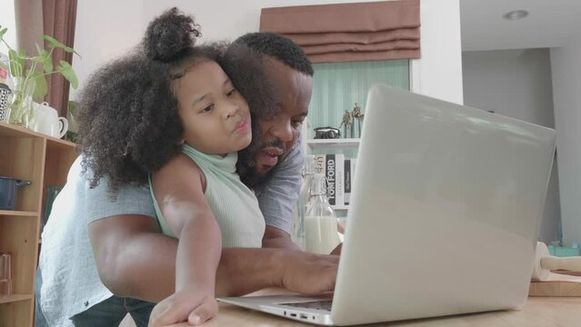 African American dad and daughter culinary lesson online with laptop at the home kitchen table