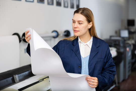 Woman, printing establishment worker, examining large piece of paper, checking results of printing.