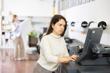 Caucasian woman working in printing office, using large format printer.