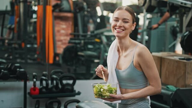 Healthy habits concept. Unrecognizable european muscular woman in sportswear sitting on a floor with her legs crossed, eating a healthy salad. High quality 4k footage