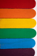 detalle de batelenguas de madera multicolor, con bandera de orgullo gay, sobre fondo blanco, pintado con pintura acrílica