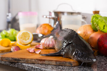 View of sturgeon fish lying on wooden board on stone surface with fresh fruits and vegetables