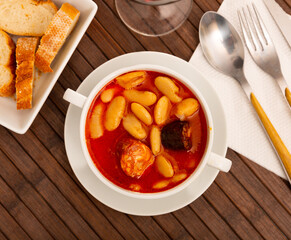 Hearty beans stew with pork, blood sausage and chorizo served in white bowl. Traditional dish of...