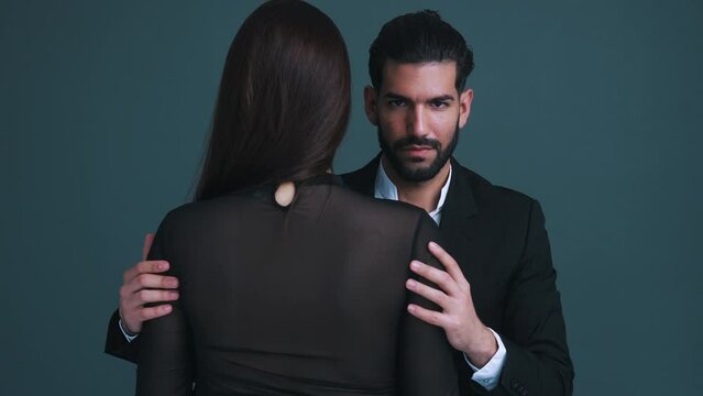 Hot seductive bearded man in a suit holding tightly his long-haired woman with both of his hands. Gray background studio shot. High quality 4k footage