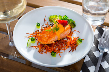 Appetizing roasted salmon steak on carrot brushwood with sauce and broccoli garnished with...