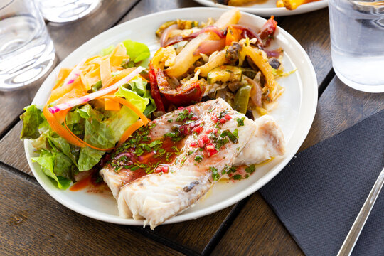 Traditional French fish dish of baked blue ling fillet with savory sauce, fresh green salad and vegetable saute..