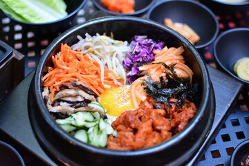 Traditioanl Korean bibimbap in hot stone bowl with pickled vegetables on the side