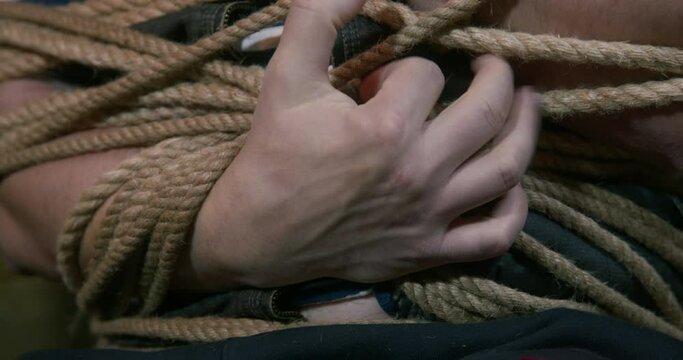 Person is tightly bound with a rope, but tries to pull out his hand to get out and escape, close up. Friendly prank or illegal kidnapping. Captured military hostage