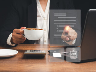 Businesswoman holding a coffee cup and working at digital documents on a virtual screen while...