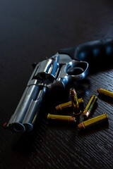 Artistic photo of a 357 magnum caliber revolver on a dark wood grain background with loose rounds of ammunition
