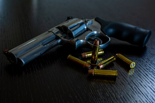 Artistic photo of a 357 magnum caliber revolver on a dark wood grain background with loose rounds of ammunition