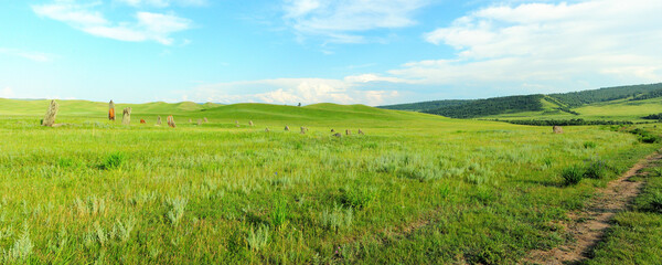 Fototapeta na wymiar Panoramic shot of a summer valley with ancient stone grave sculptures.