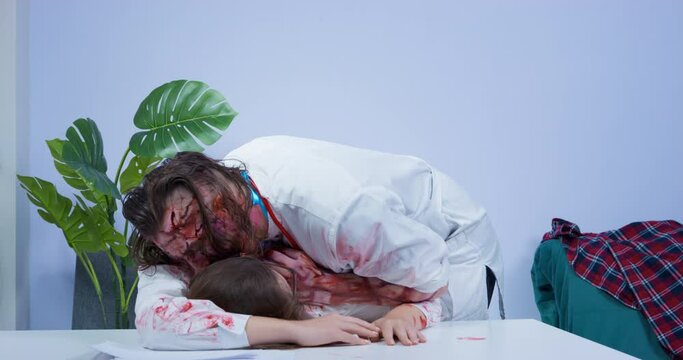 Creepy male zombie with bloody face and in medical uniform with stethoscope around his neck attacked woman, and now eats her. Halloween themed zombie apocalypse party