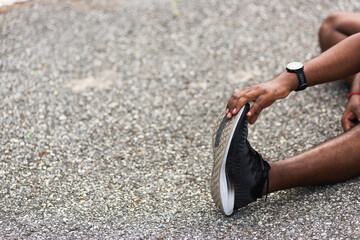 Close up Asian young athlete sport runner black man wear watch he sitting pull toe feet stretching legs and knee before running at outdoor street health park, healthy exercise before workout concept