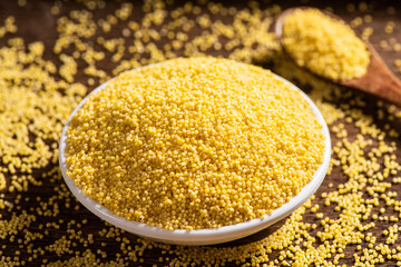 Raw dry millet in a plate on wooden table.