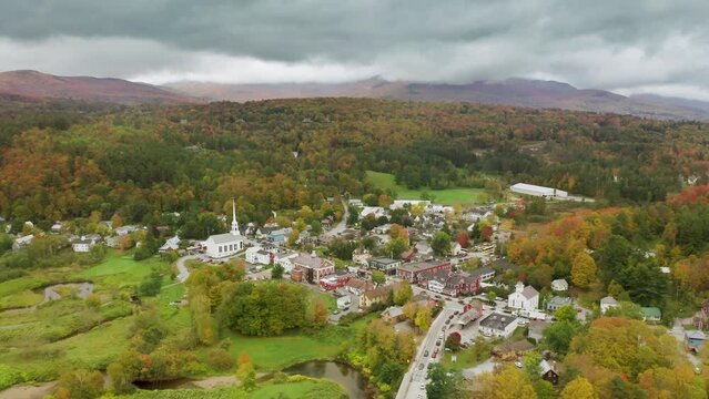 East Coast Vermont landscapes USA. Small countryside village with white church on scenic fall foliage forest landscape background. Cinematic 4K aerial white wooden old historic Stowe community church