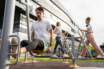 Group of friends man and women male and young adult people training at outdoor open gym in park in front of modern building real people sport and recreation exercise healthy lifestyle concept - Powered by Adobe