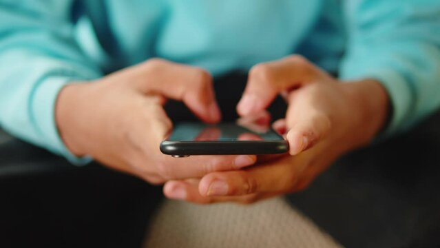 African American man using smartphone. Young guy texting at phone, teenager relaxing at home. Communicating with family and friends online, sitting on sofa in living room.