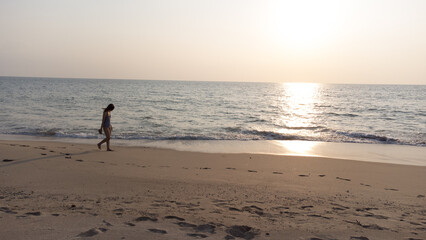 Naklejka premium Happy Carefree Woman Enjoying holiday. Woman silhouette walking on the beach at sunset. 