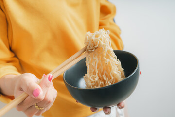 Asian girl holding a bowl of noodles with chopsticks and eating it, isolated on white background