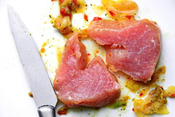 cut pieces of raw red marinated meat with spices cooked for roasting for lunch and kitchen knife on a white background