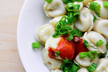 meat dumplings cooked with red tomato sauce and green onions on plate close up