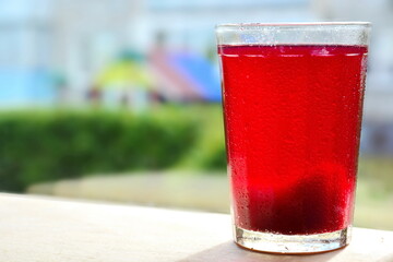 Glass with spray of water drops with bright red sweet fruit berry refreshing cool drink on window on blurred background
