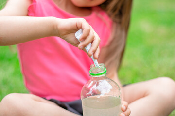 Obraz na płótnie Canvas Drink with electrolytes in a transparent bottle in the hands of a happy child on a green lawn in a pink T-shirt