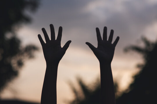Silhouette of two hands raise with blurred sunset sky background