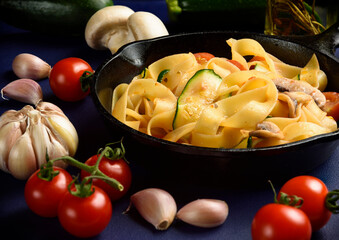 Fettuccine, Italian pasta, with mushroom, garlic, cherry tomato and cucumber in tomato sauce cooked in cast iron pan, moody shot