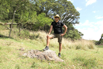 Latin adult man with sunglasses, hat and backpack celebrates that he managed to climb the mountain, he feels full, happy, enthusiastic, free celebrates his achievement
