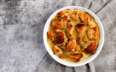 Oven baked chicken with potatoes in sour cream in a white baking dish on a dark grey background. Top view, flat lay