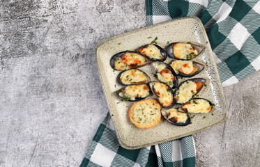 Baked mussels with cheese and herbs  on a square  plate on a dark background. Top view, flat lay