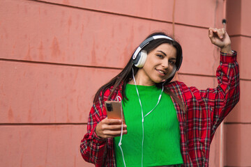 young latin hispanic man with headphones and phone dancing in the street