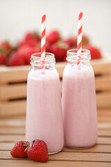 Cocktail from milk and ripe strawberry on wooden table on background of box full of berries