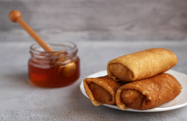 thin pancakes envelope filled with cottage cheese and raisins on a saucer with honey on a gray background