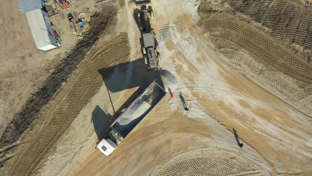 Above top view, overhead on tipper truck as lifting his trailer to unload cargo, fraction, small crushed stone for new circular road, roundabout under construction.

