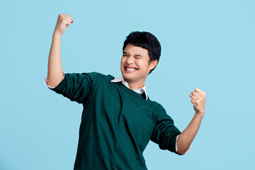 Portrait of a cheerful young Asian man in casual clothes. He raised his fist with a happy smile on...