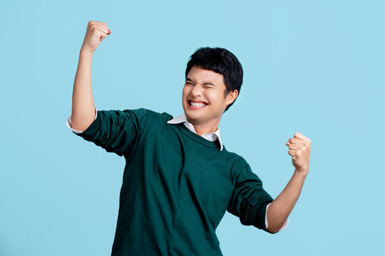 Portrait of a cheerful young Asian man in casual clothes. He raised his fist with a happy smile on his face as a gesture of celebration.