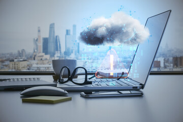 Close up of laptop on workplace with city view, items and abstract hologram raining cloud on blurry...