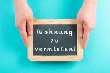 Holding a chalkboard in the hands, apartment for rent is standing in german language on the sign,...