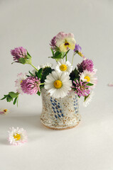 Small bouquet of wild flowers in a vase on a gray background. Daisies, clover, pansies. Selective focus on a daisy, natural light. vertical image