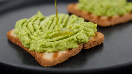 Cooking avocado toast. Pour oil over mashed avocado on toasted bread. Vegan food concept