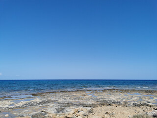The coast of the Mediterranean Sea, long frozen lava, in the recesses of which there is sea water against a blue sky.