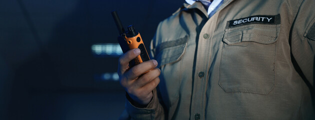 Professional security guard with portable radio set in dark room, closeup. Banner design