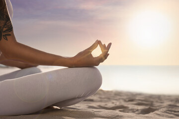 Fototapeta na wymiar Young woman meditating on beach at sunrise, closeup. Practicing yoga