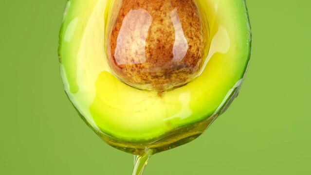 Avocado. Half raw fresh organic green avocado fruit with oil stream isolated on green background