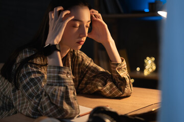 Female student studying at home getting headache at night. Tired girl and college education feel...
