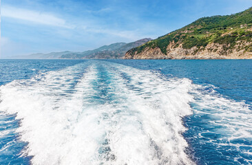 A wave from a cruise boat on the surface of the water, a horizon with a blue sky and villages Cinque terre. Ligurian coast of Italy.