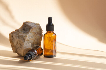 Two mockup bottles with dropper caps made of amber glass for serum next to a marble stone....